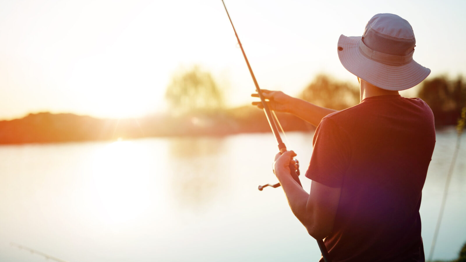 Young man fishing on a lake at sunset and enjoying hobby and recreation